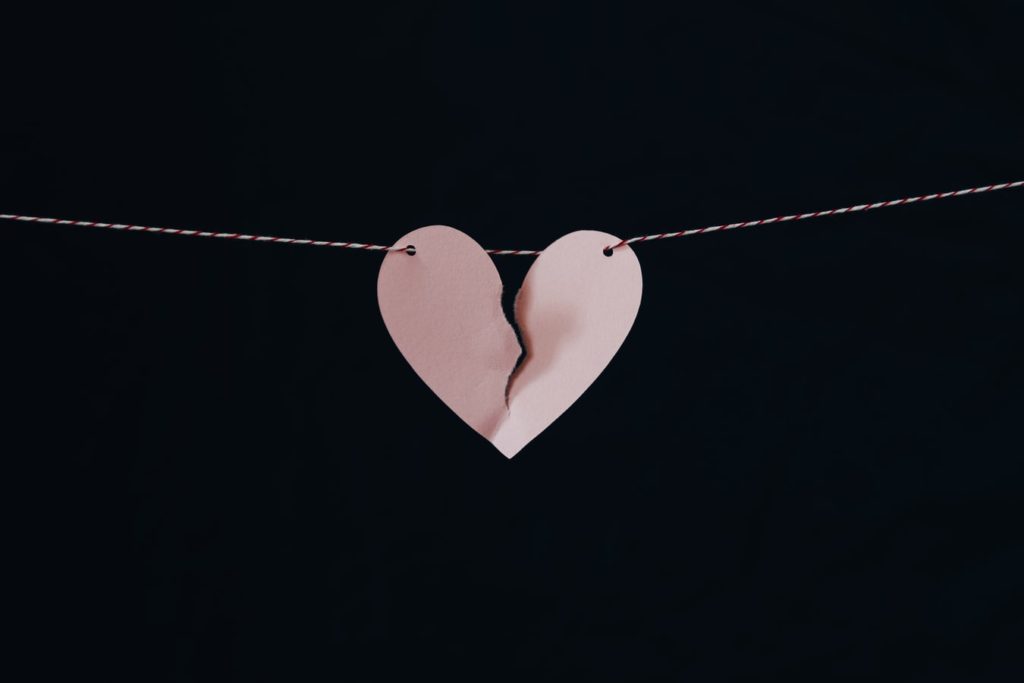 A paper heart dangling from a string with a rip down the middle signifying a broken heart.