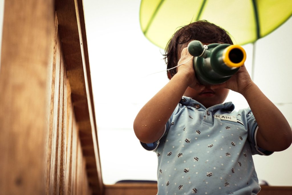 A small curious child looking through a toy to discover the world.