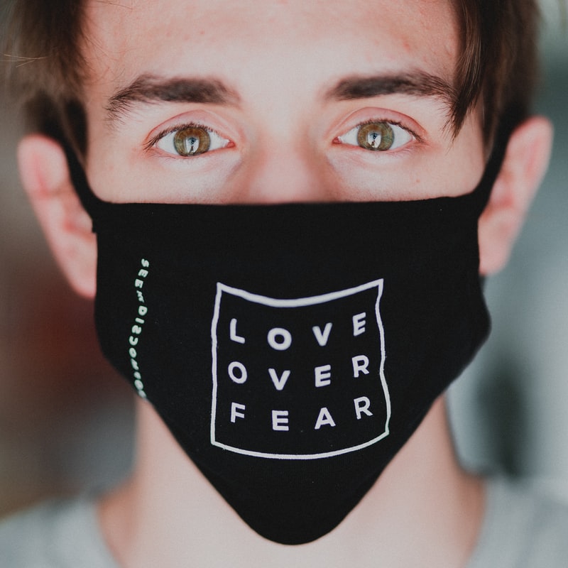 A man is looking directly into the camera wearing a mask with LOVE OVER FEAR printed on the mask.