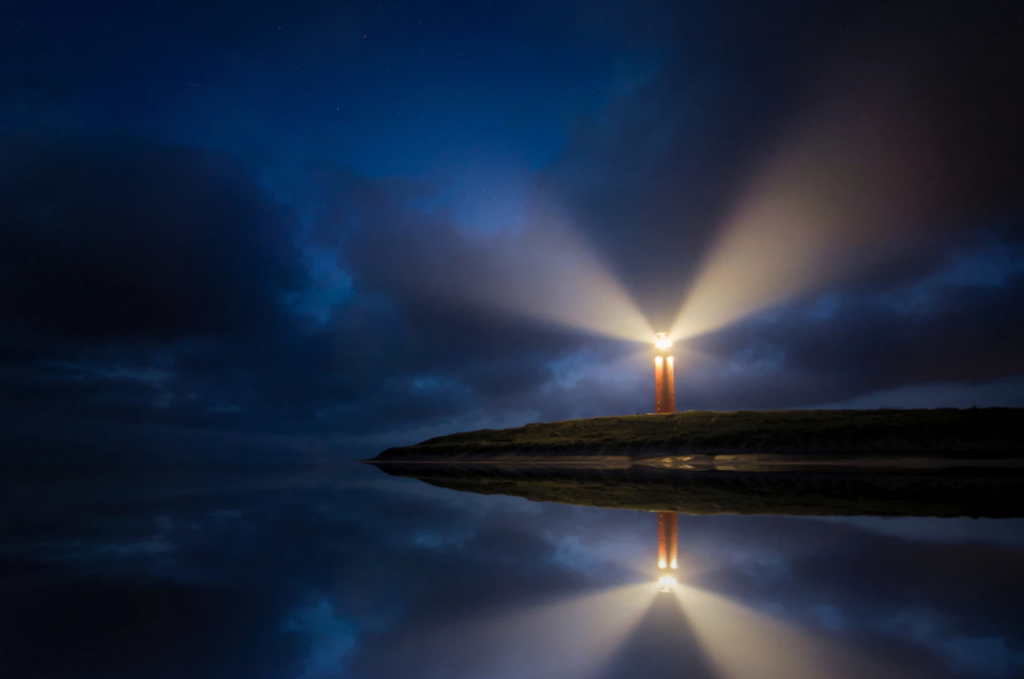 Lighthouse in the dark reflecting off the still water.