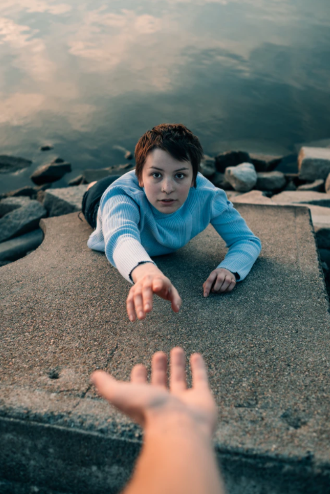 A hand reaching to help another person climb a steep incline. 